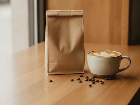 A bag of coffee beans and a latte on a wooden counter